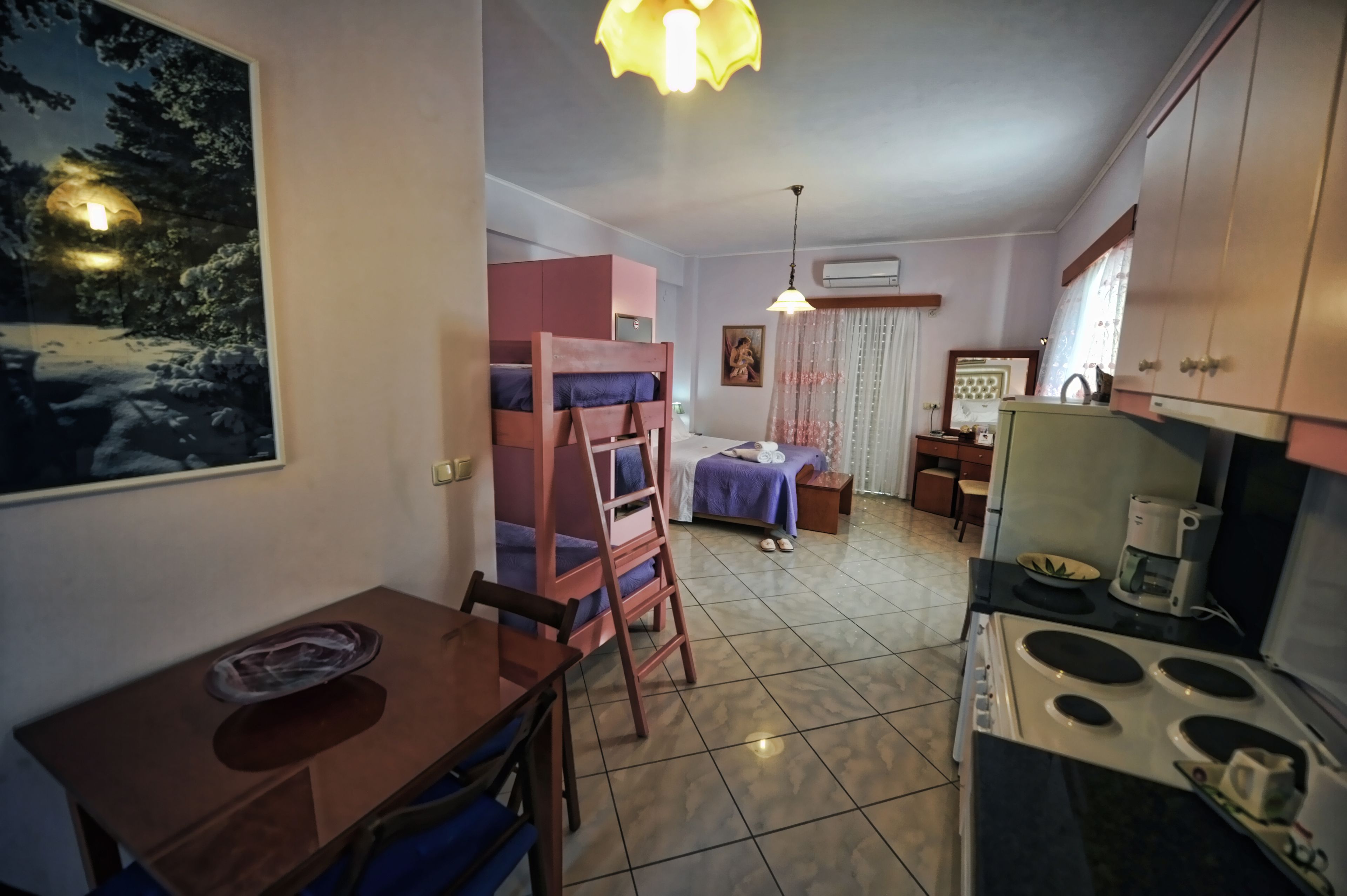 Una habitación compacta con literas, una mesa de comedor, una zona de cocina con estufa y un cuadro de un paisaje nevado.