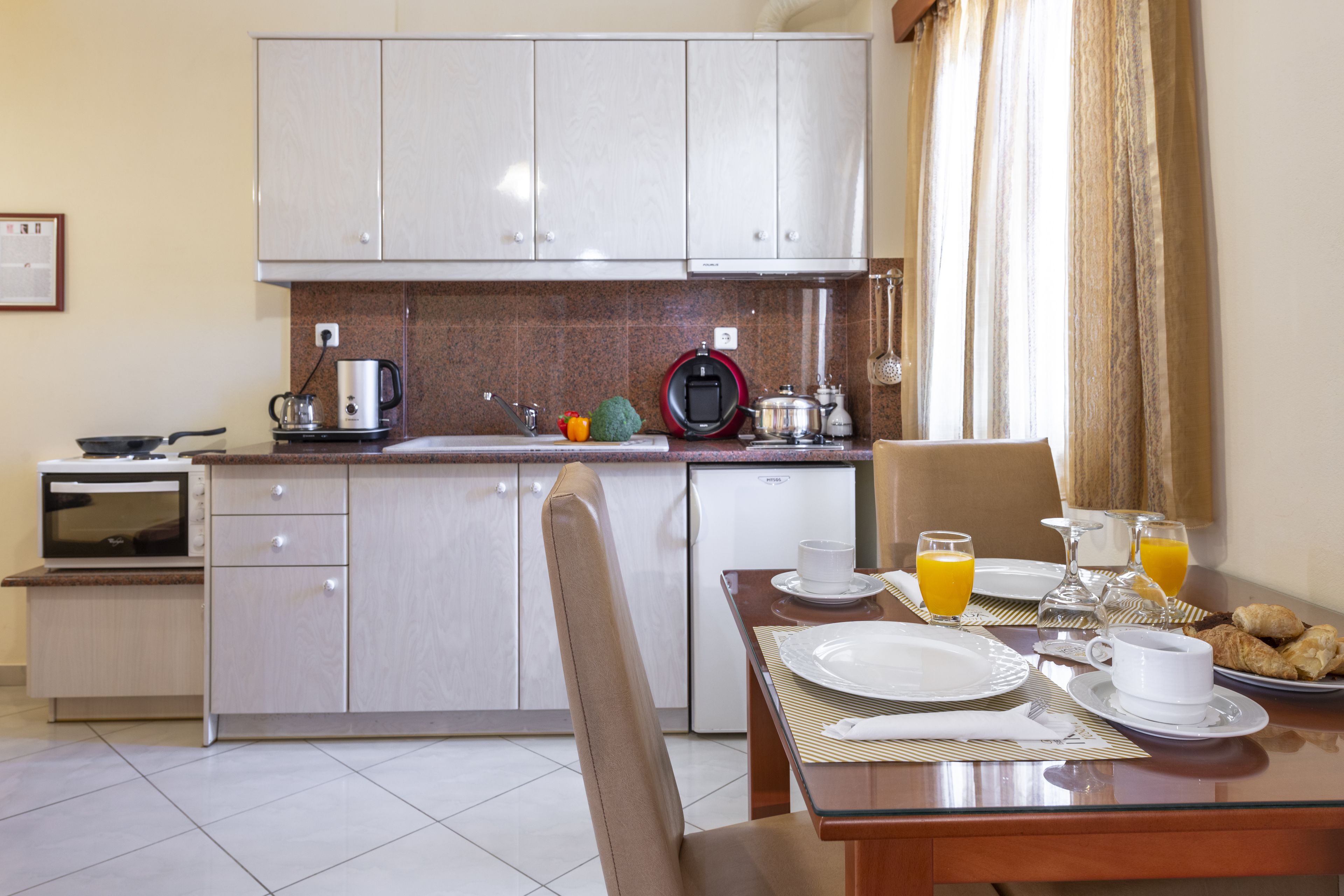 A modern kitchen with white cabinets, a dining table set with plates, cups, and a fruit bowl.