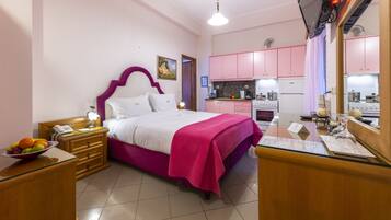 A bedroom with a bed, bedside table, and a small kitchen area with pink cabinets and a stove.