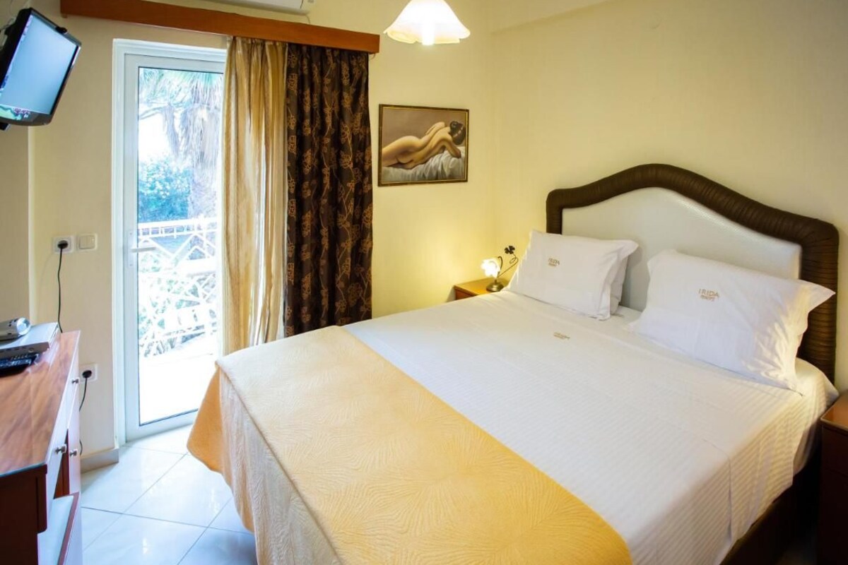 Quarto de hotel com uma cama grande, uma escrivaninha com computador, televisão e vista para o exterior por uma porta deslizante.