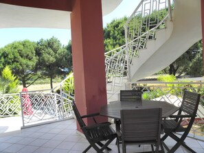 An outdoor patio with a table and chairs, a staircase, and a view of trees.