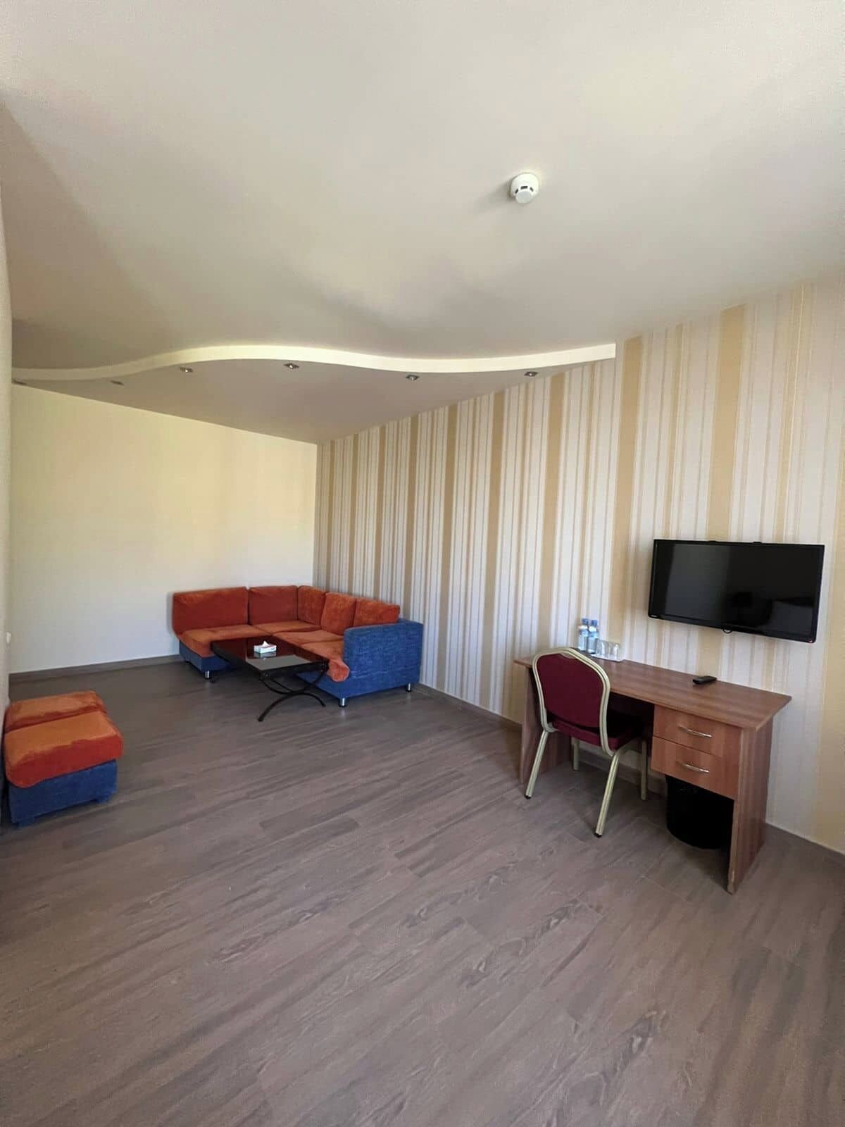 Ein modernes Wohnzimmer mit Sofa, Hocker, Fernseher und Schreibtisch.