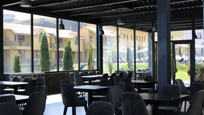 A spacious indoor dining area with multiple tables and chairs, large windows offering views of buildings and greenery outside.