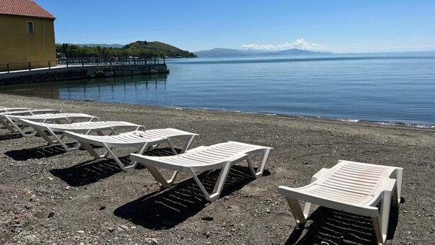 A beach with white lounge chairs and a yellow building.