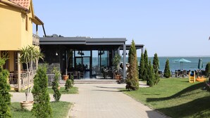 A coastal restaurant with outdoor seating, a paved walkway, and a view of the sea.