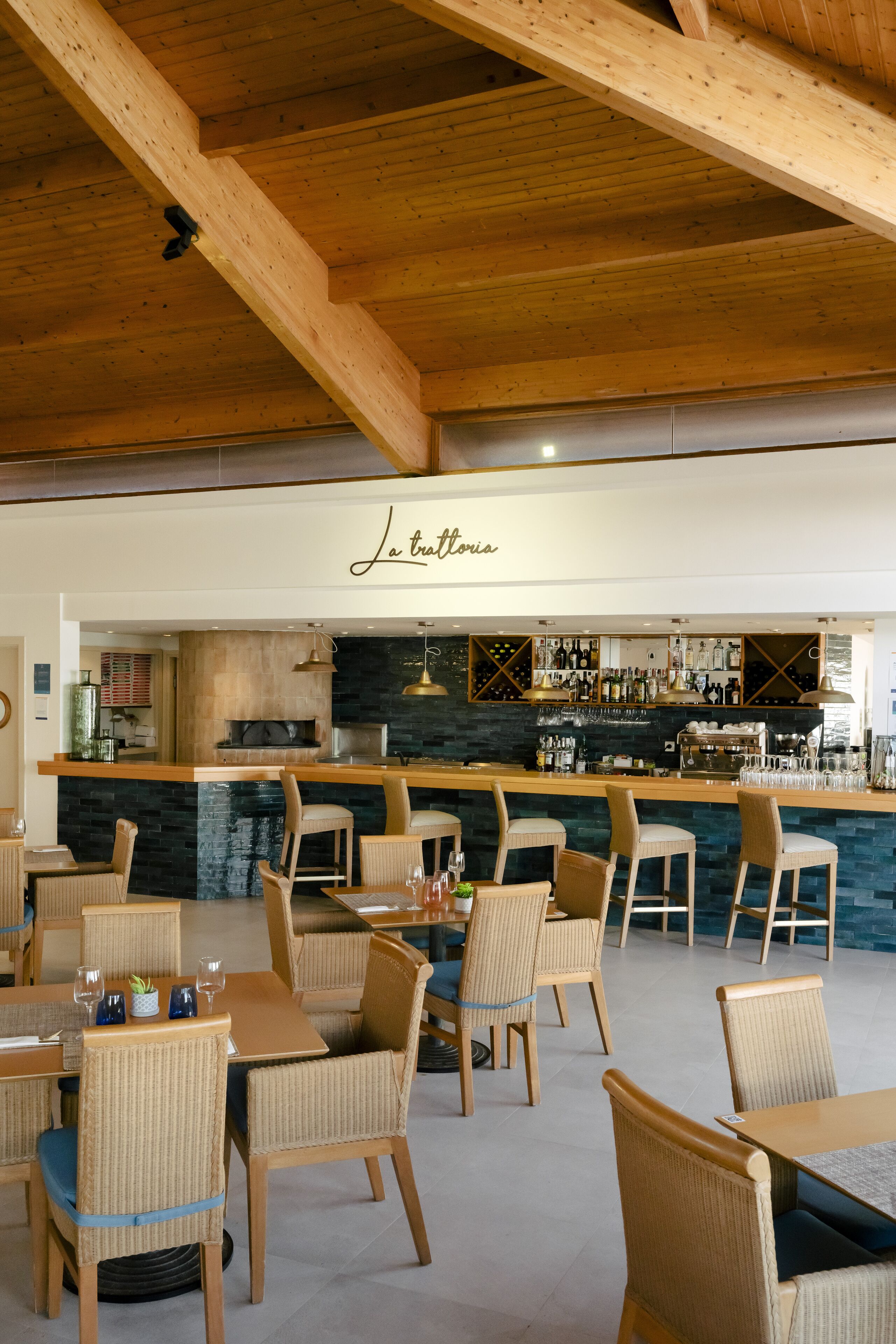 A restaurant with wooden beams, wicker chairs, and a bar area with a stone countertop.