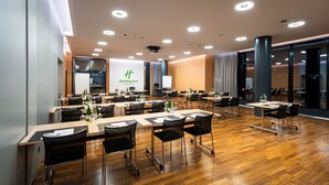 Uma sala de conferência com várias mesas e cadeiras, uma tela grande e uma placa da Holiday Inn.
