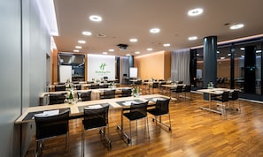 A conference room with multiple tables and chairs, a large screen, and a sign for Holiday Inn.