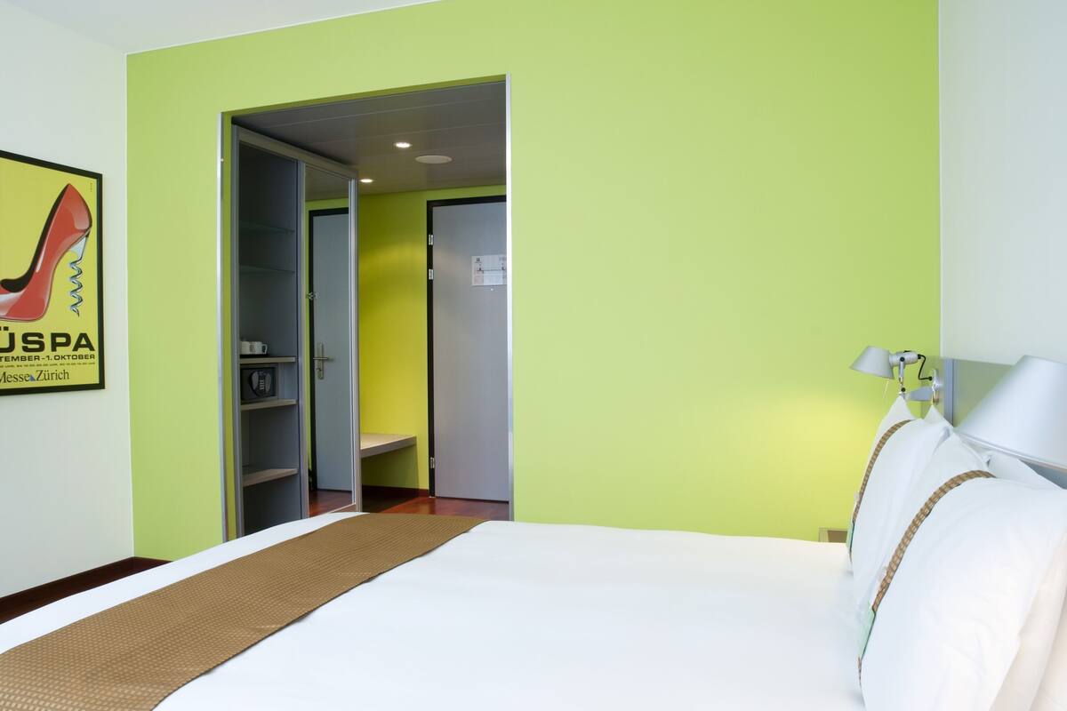 Ein Hotelzimmer mit Bett, Nachttisch, Lampe und Kleiderschrank.