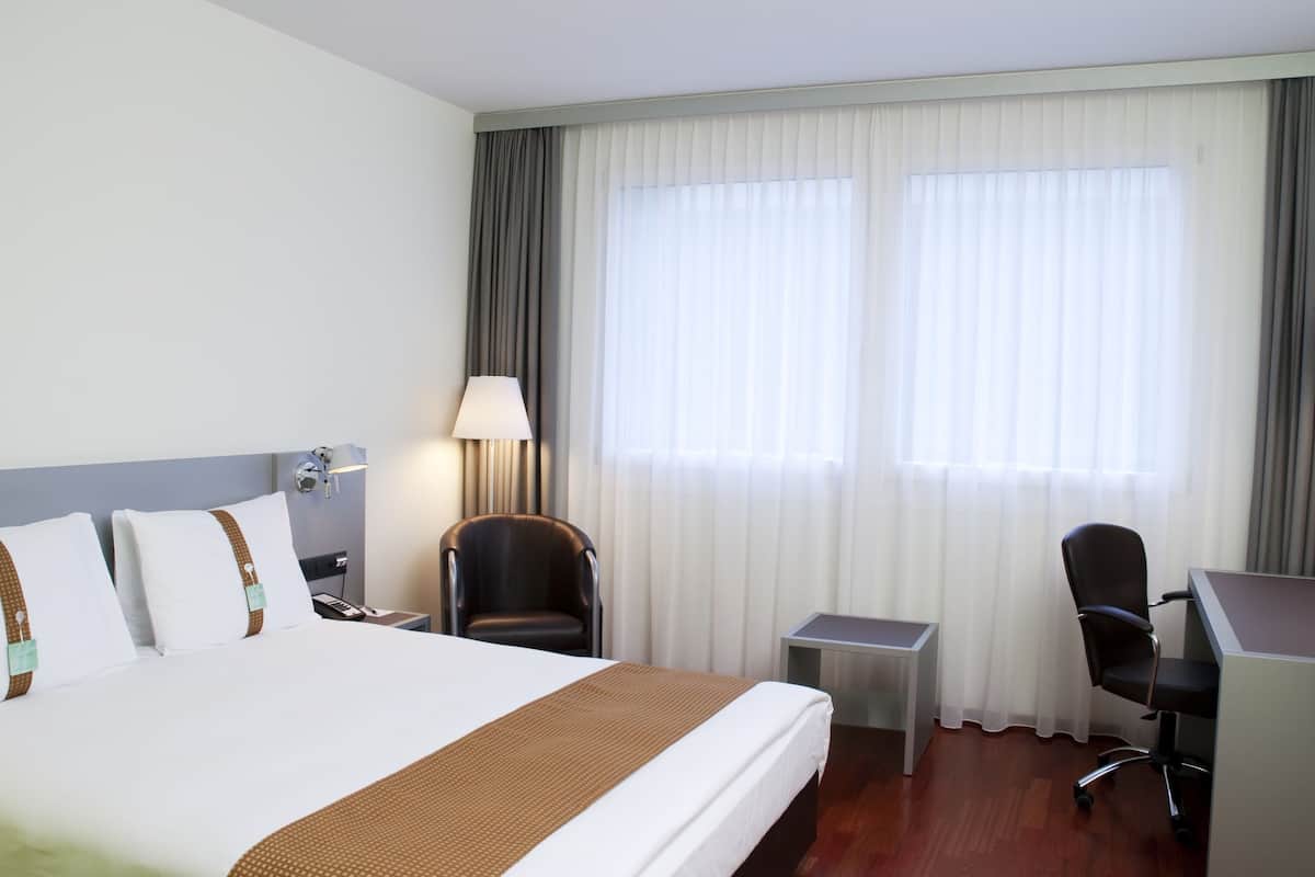 Ein Hotelzimmer mit einem großen Bett, einem Schreibtisch, einem Stuhl und einer Lampe.