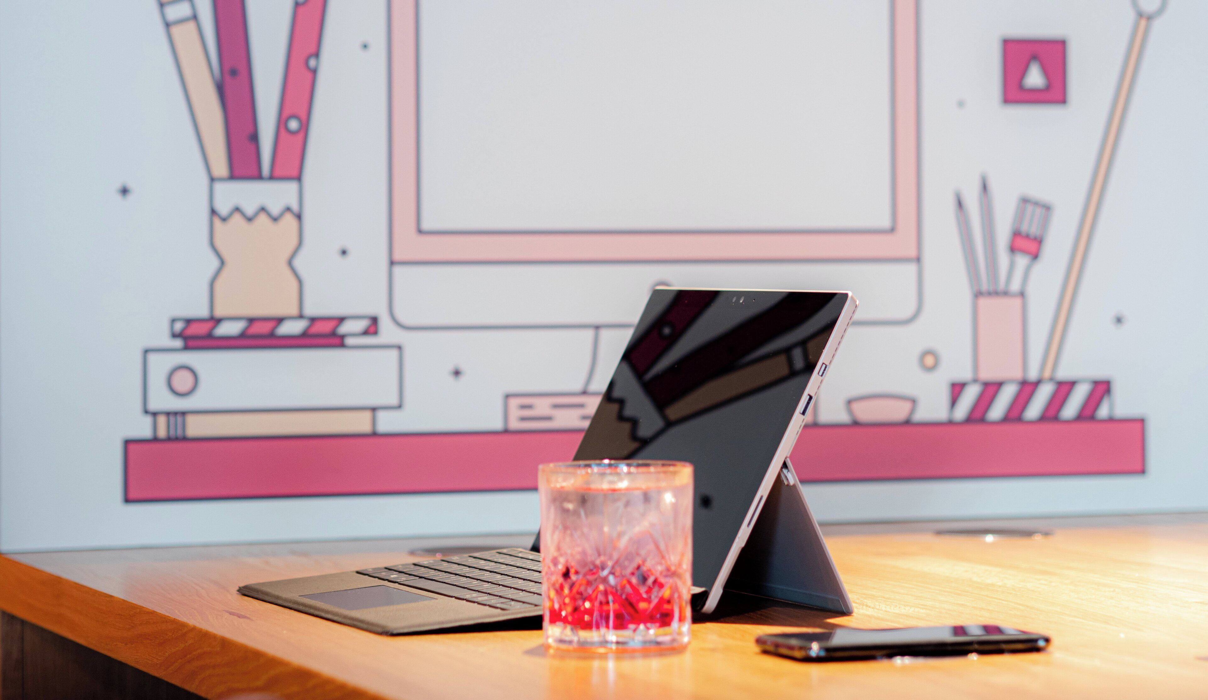 Un ordinateur portable posé sur un bureau en bois, avec un verre rempli de billes rouges, un smartphone et une tablette.