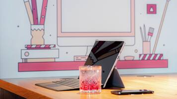 Un ordinateur portable posé sur un bureau en bois, avec un verre rempli de billes rouges, un smartphone et une tablette.