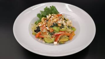 Un plato blanco con un plato de fideos, adornado con vegetales y nueces, sobre una superficie negra.