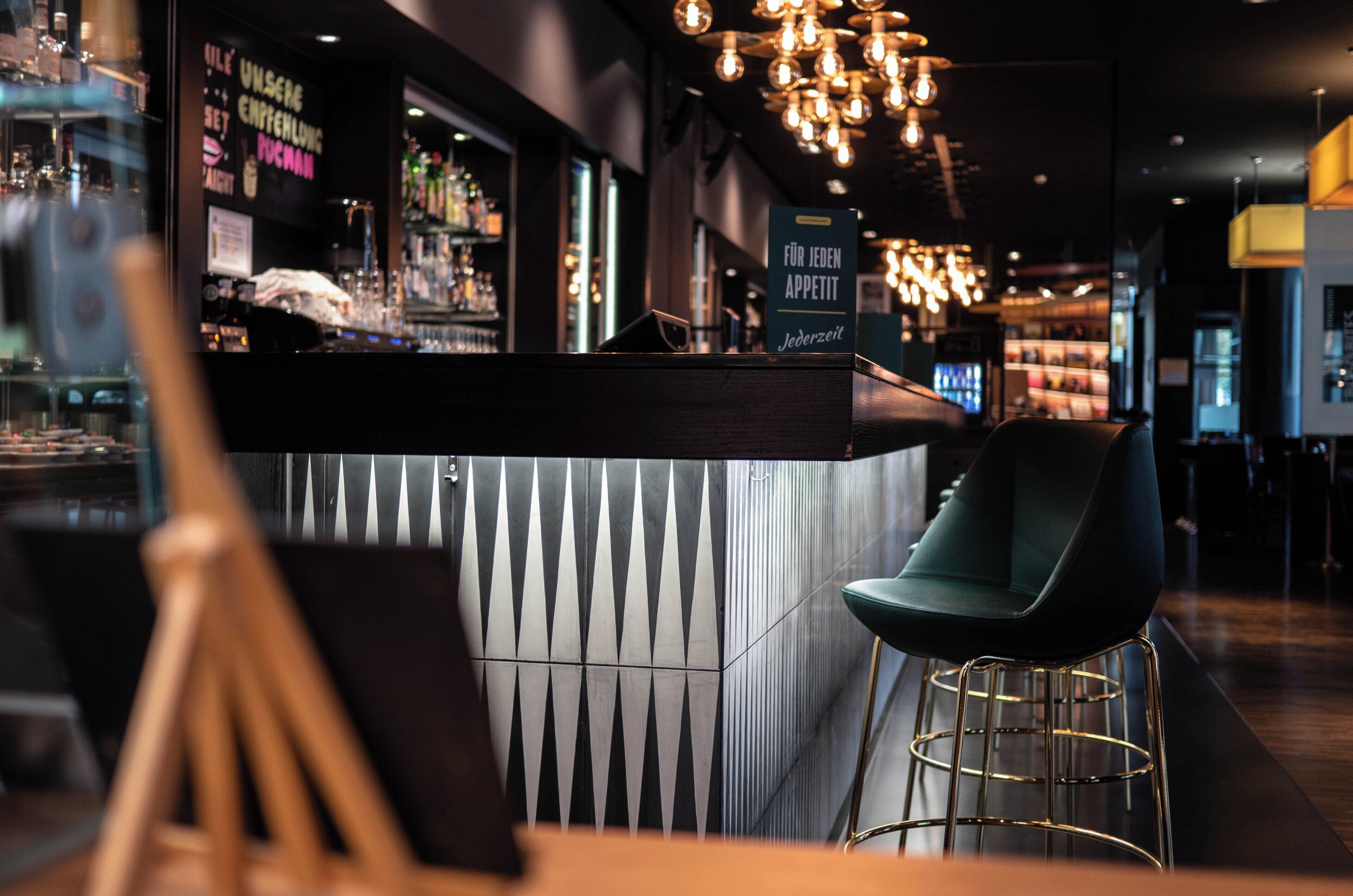 Un espace bar moderne avec un comptoir, des tabourets de bar et un luminaire suspendu.