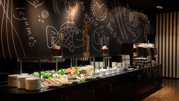 Uma área de buffet com diversos alimentos e uma parede de lousa com desenhos relacionados à comida.