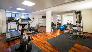 Academia com equipamentos de exercício, piso de madeira e janelas amplas.