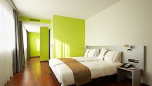 Quarto de hotel com uma cama grande, uma mesa de cabeceira com telefone e uma parede verde vibrante.
