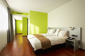 A hotel room with a large bed, a bedside table with a phone, and a bright green accent wall.
