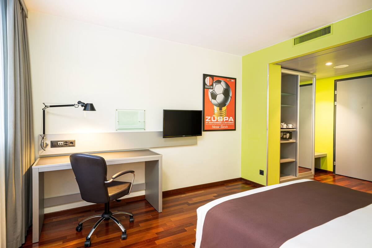 Ein Hotelzimmer mit Bett, Schreibtisch, Stuhl, Fernseher und einem Bild an der Wand.