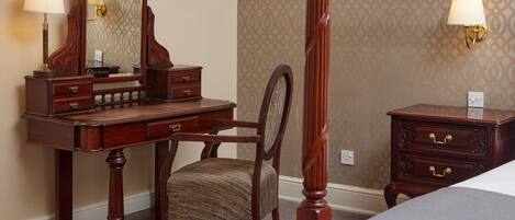 A bedroom with a wooden four-poster bed, a wooden desk with a chair, a dresser, and a nightstand with a lamp.