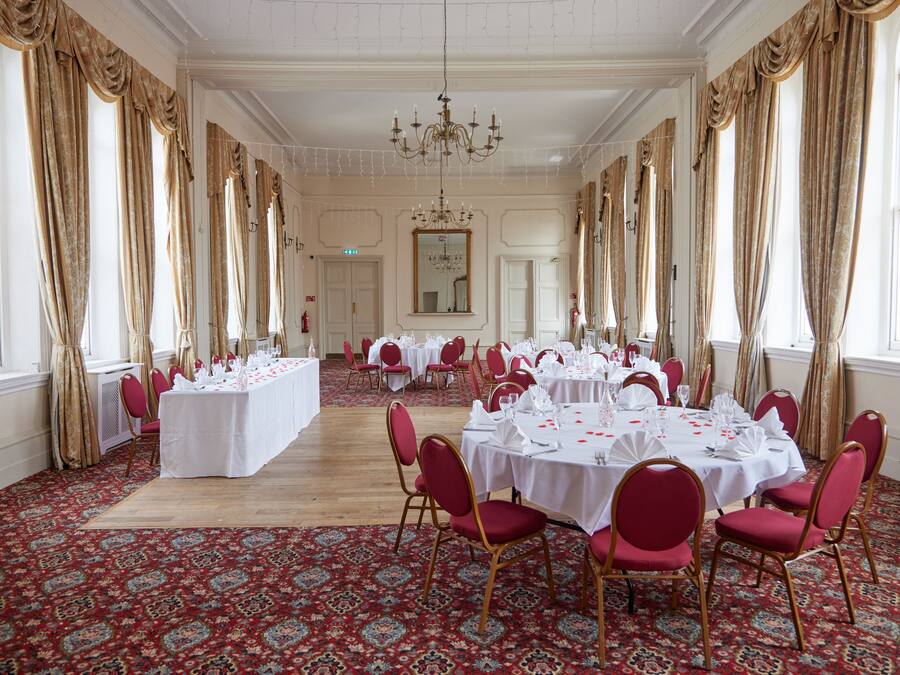 A banquet hall with tables set for a formal event, featuring a patterned carpet and red chairs.