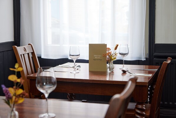 A dining table with a menu, wine glasses, and a vase with flowers.