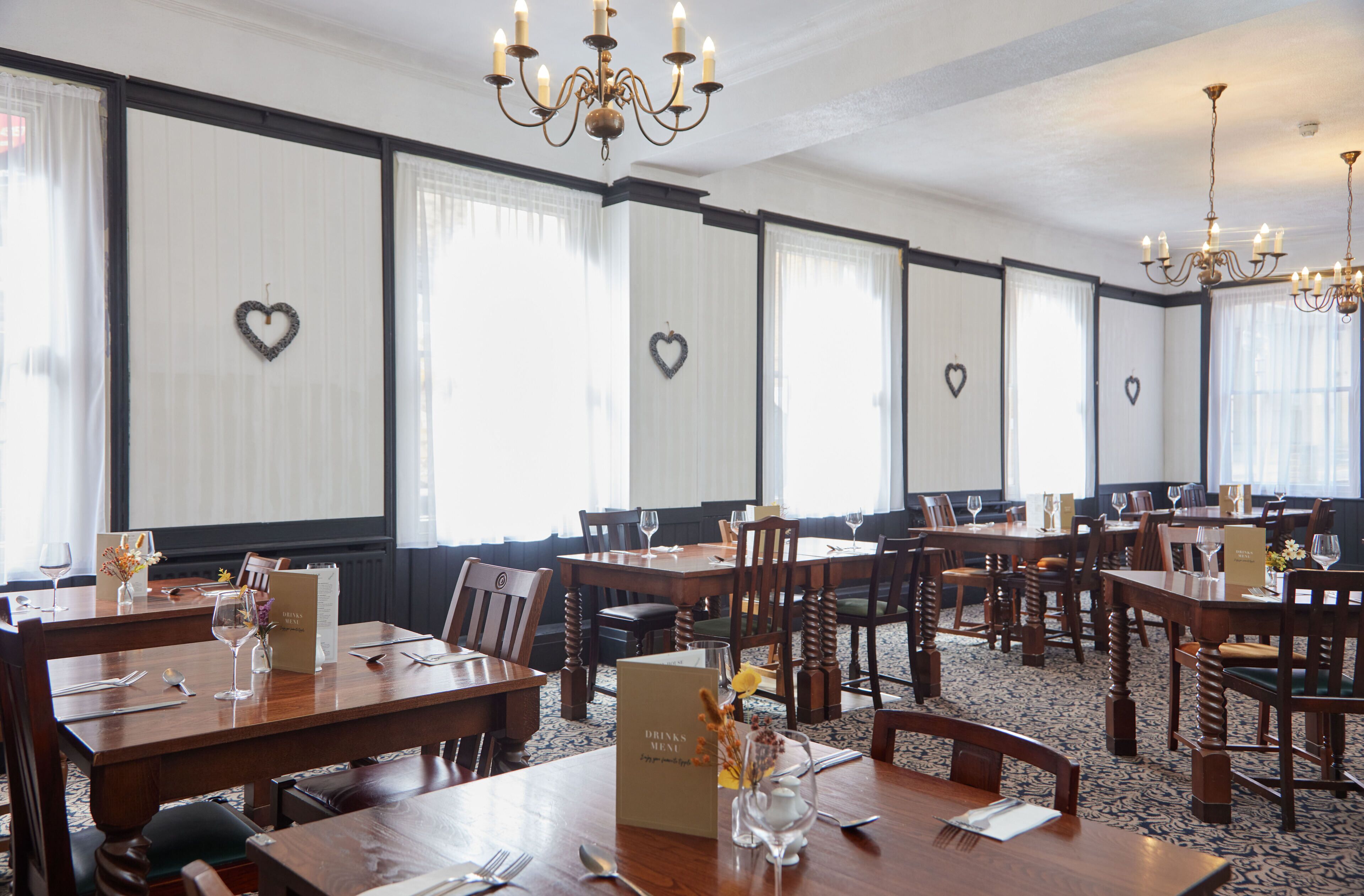 Ein Hotelrestaurant mit mehreren Holztischen und -stühlen, Kronleuchtern und herzförmigen Dekorationen an den Wänden.