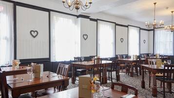 Ein Hotelrestaurant mit mehreren Holztischen und -stühlen, Kronleuchtern und herzförmigen Dekorationen an den Wänden.