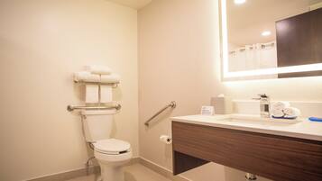 Een moderne badkamer met toilet, handgrepen, een wastafel met spiegel en een handdoekhouder.