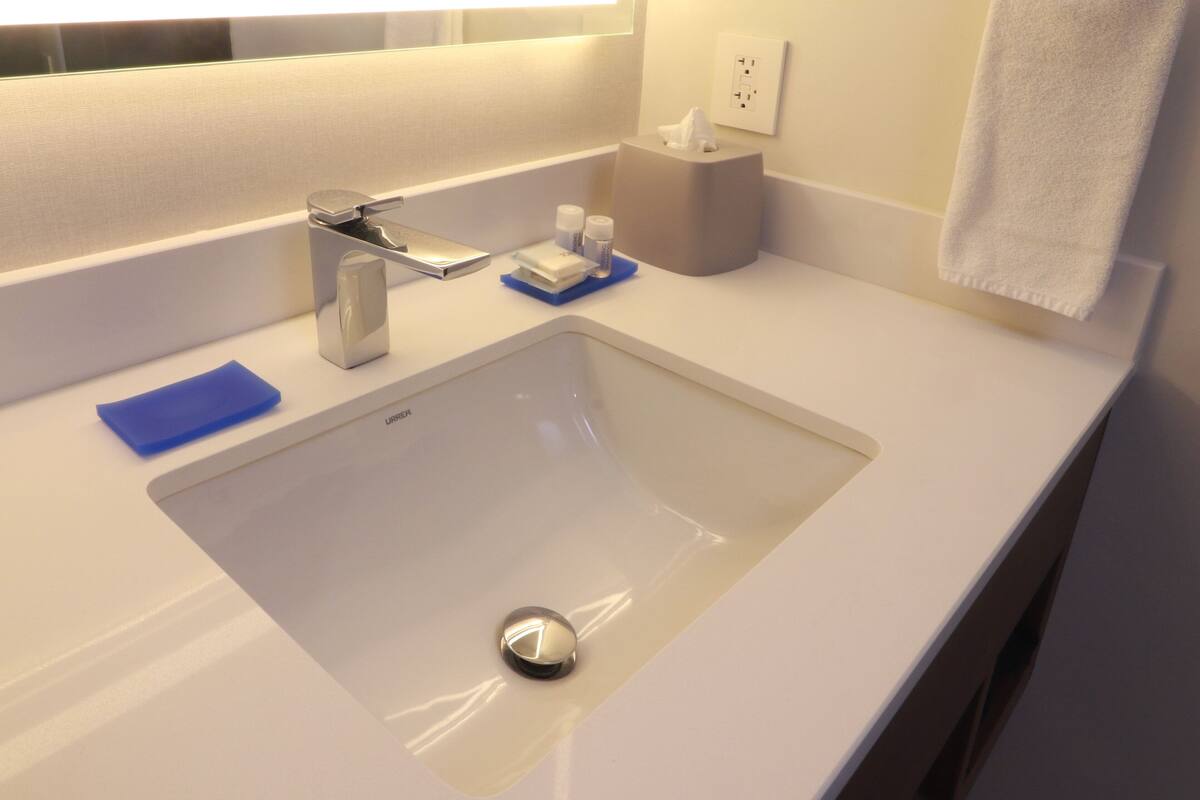 A modern bathroom with a white sink, a mirror, and a towel hanging on the wall.