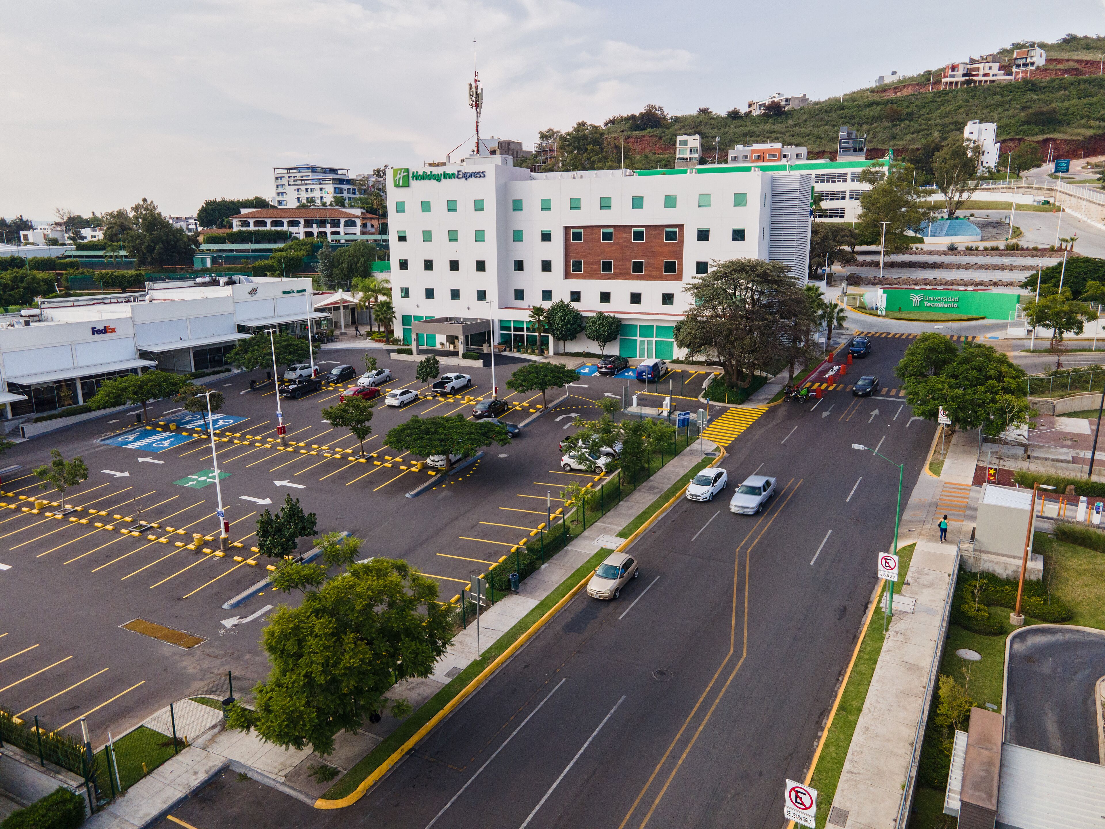 Un edificio a più piani con facciata verde e bianca, un parcheggio con posti delimitati e una strada con veicoli.