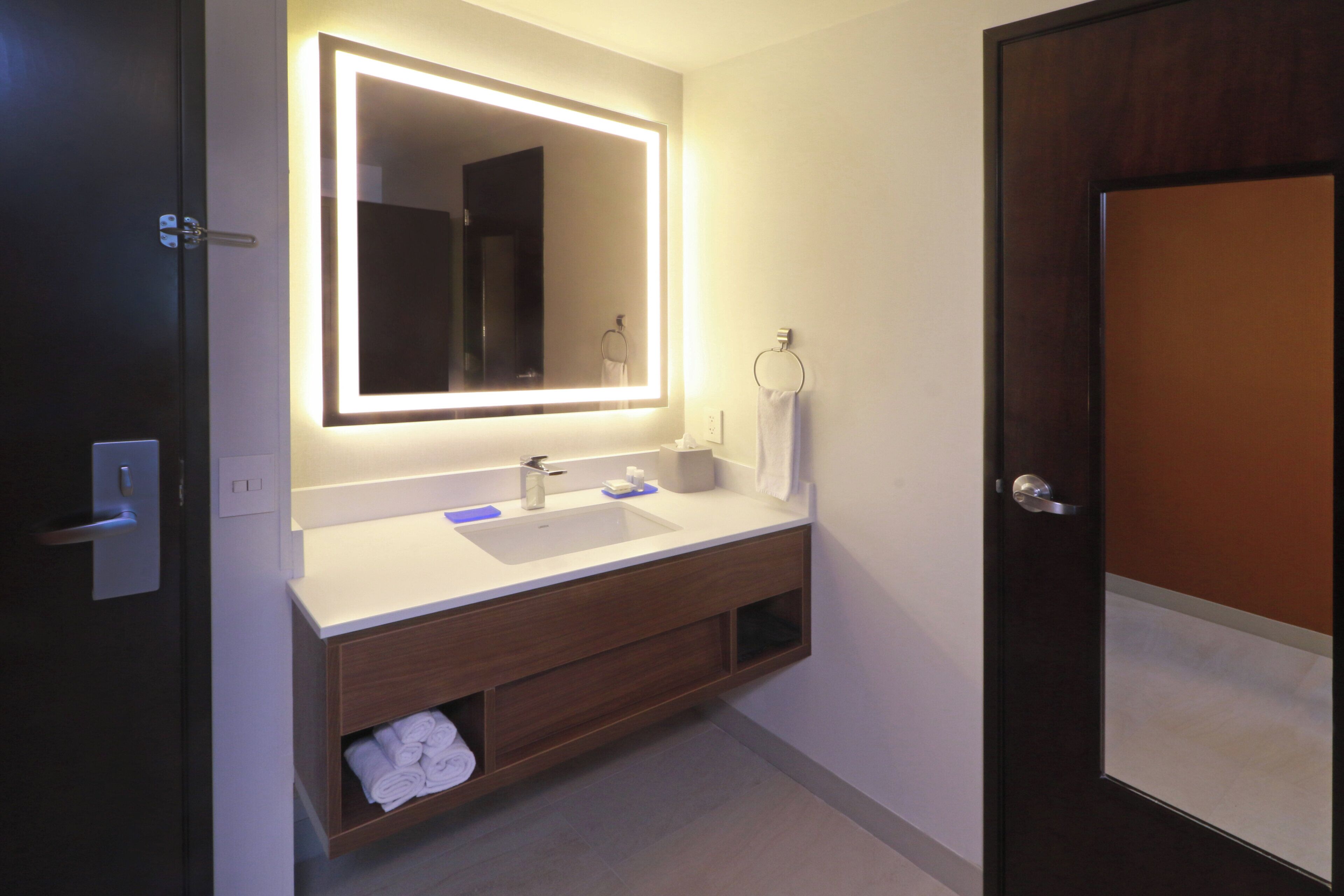 A modern bathroom with a large mirror, a sink, and a towel rack.