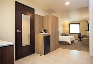 A hotel room with a wooden wardrobe, a small kitchenette, a bed, a desk, and a television. - Holiday Inn Express Guadalajara Iteso by IHG (Tlaquepaque)
