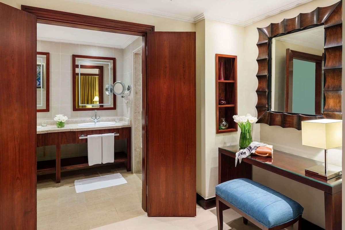 Une salle de bain d’hôtel avec un meuble-lavabo en bois, un miroir, un évier et un banc.