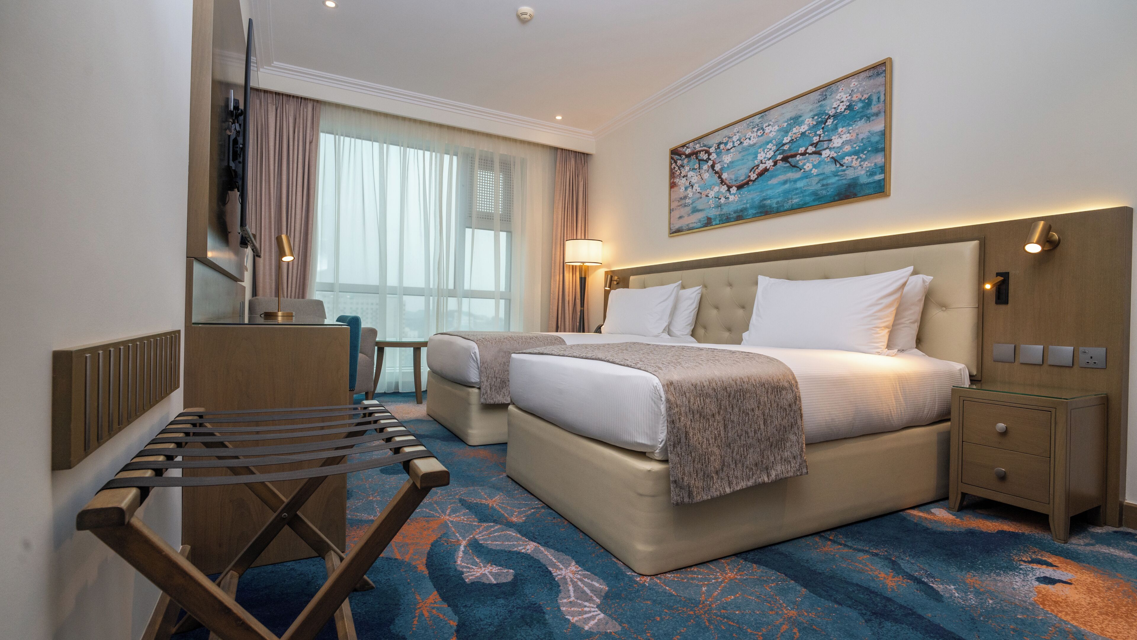 A hotel room with a bed, a desk, a chair, a TV, and a painting on the wall.