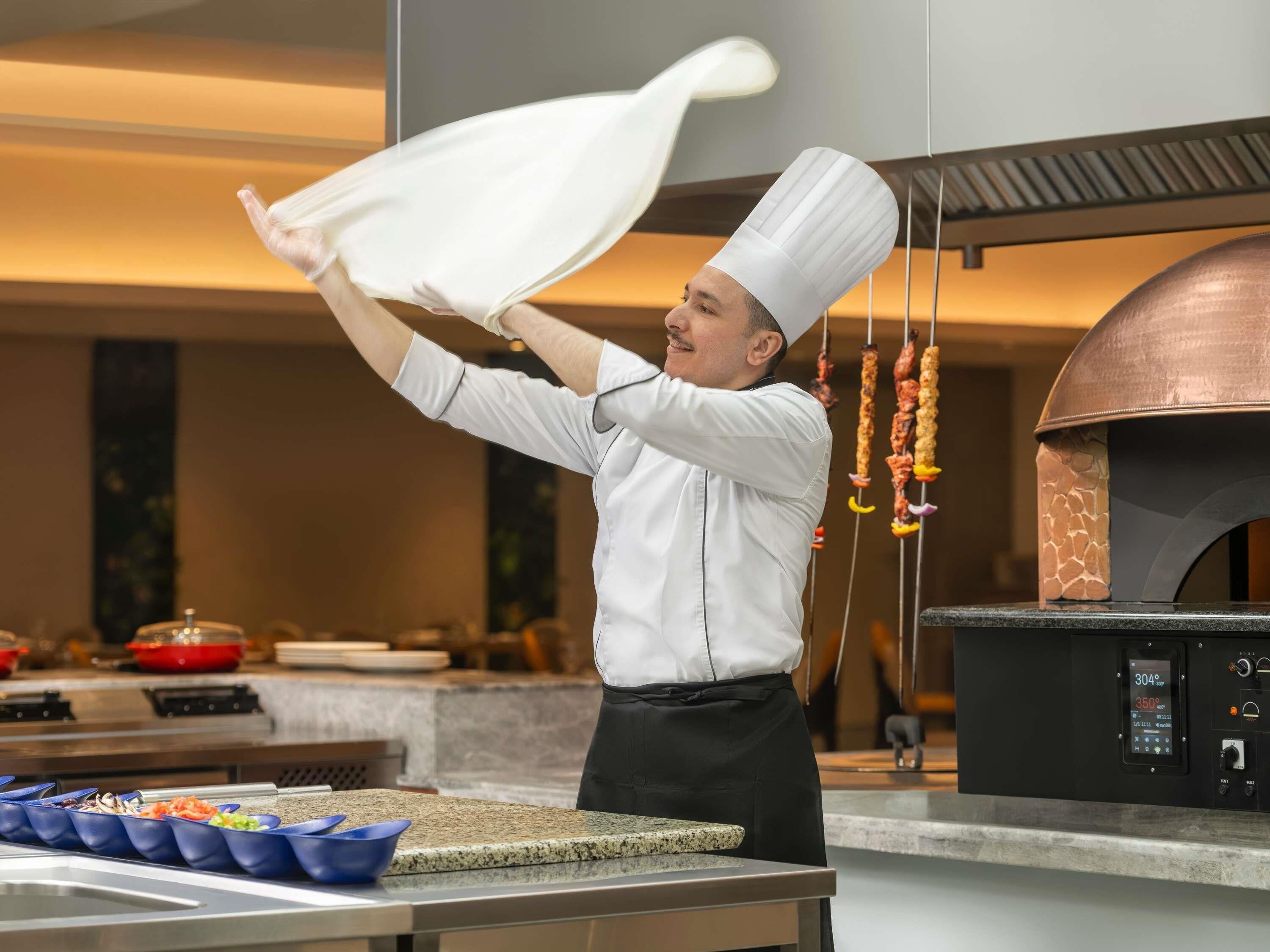 Un chef en una cocina profesional con un horno de pizza y varios utensilios de cocina.