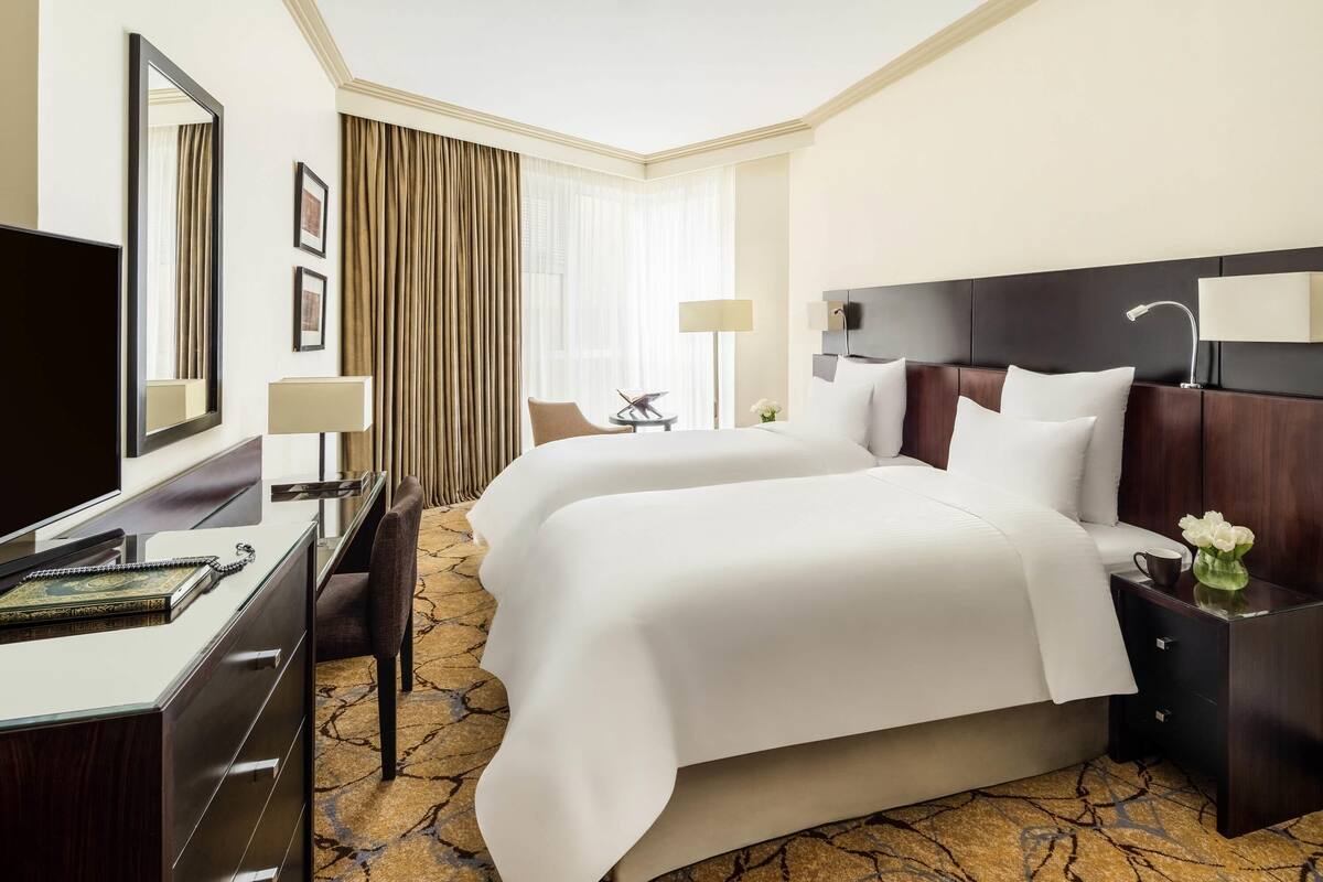 Une chambre d’hôtel avec deux lits, un bureau avec une chaise, une télévision et une table de chevet avec une lampe.