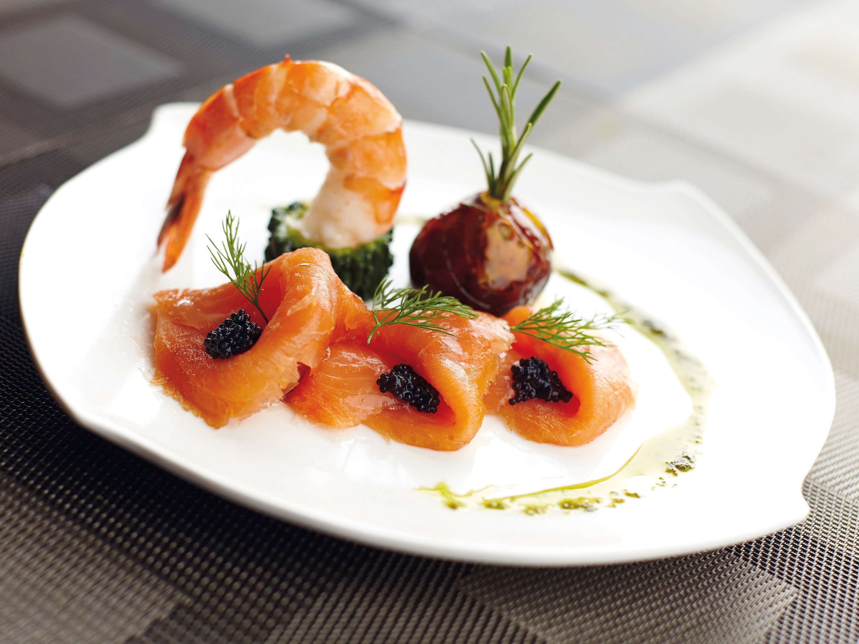 A plate of food with salmon, shrimp, and caviar, garnished with dill.