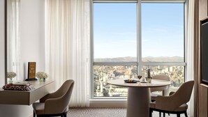 Habitació d'hotel moderna amb una finestra gran, una taula rodona, dues cadires, un televisor i un objecte decoratiu a l'escriptori.