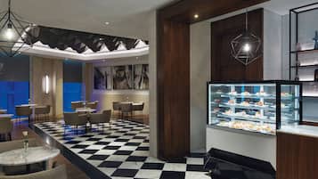 Un hall d’hôtel moderne avec un sol à carreaux, un espace salon et un présentoir de desserts.