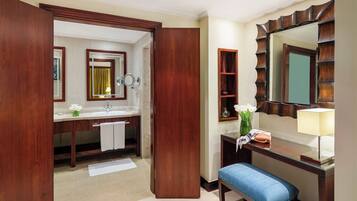 A hotel room with a wooden vanity, a mirror, a sink, a bench, and a large mirror with a decorative frame.