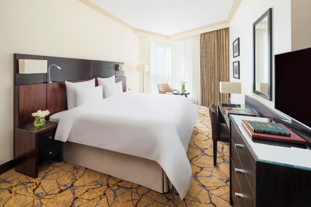 A hotel room with a large bed, a desk with a chair, a TV, and a window with curtains.