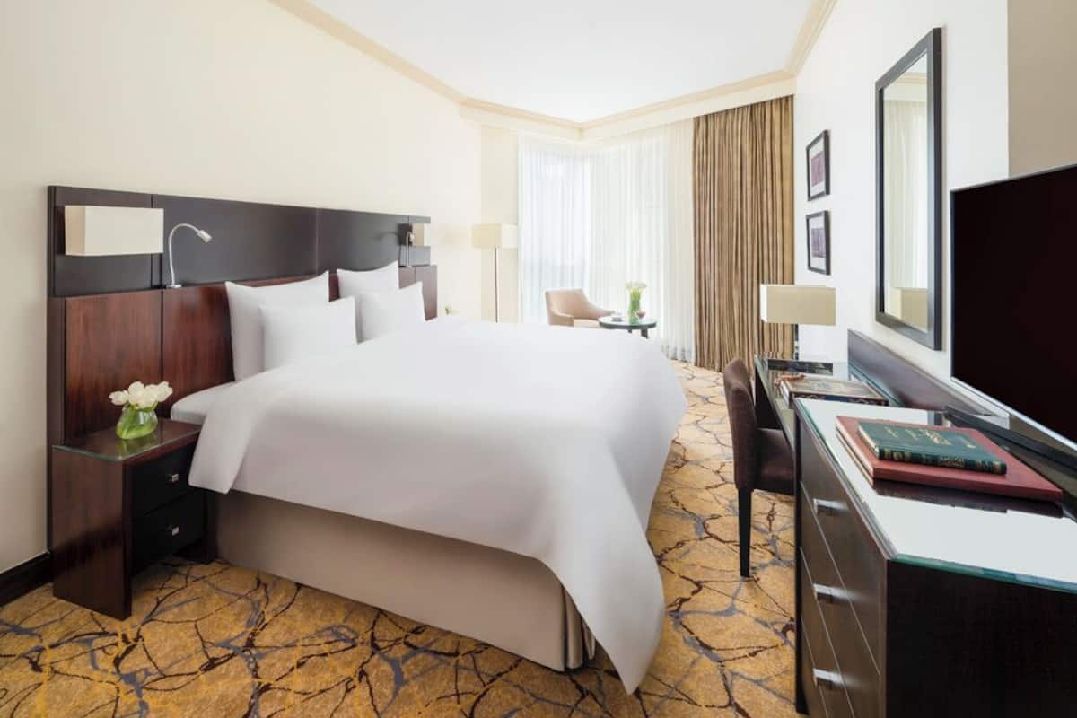 Une chambre d’hôtel avec un grand lit, un bureau avec une chaise, une télévision et une fenêtre avec des rideaux.