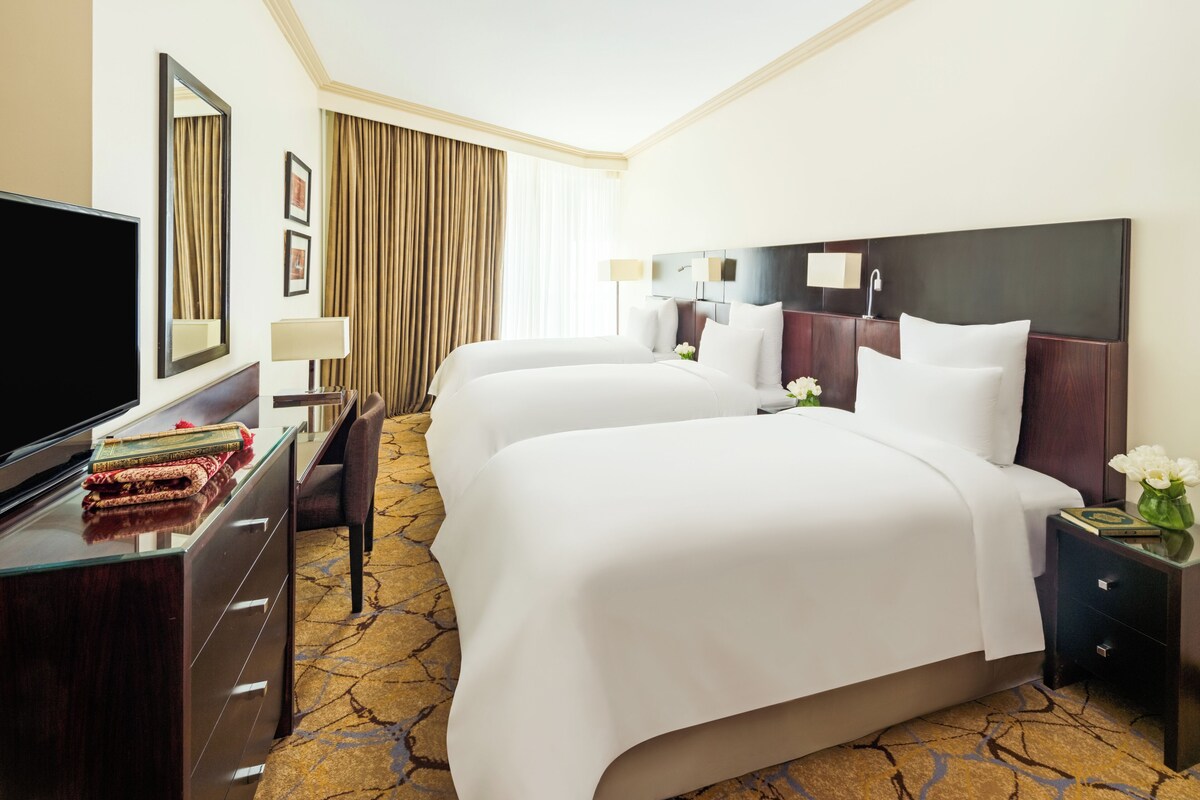 A hotel room with two beds, a TV, a desk, and a chair.