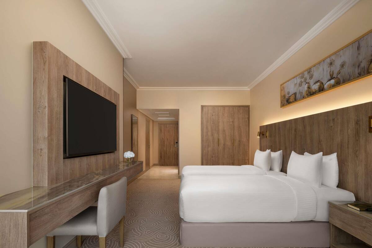 Une chambre d’hôtel avec un grand lit, un bureau doté d’un téléviseur à écran plat, une tête de lit ornée d’un tableau et une moquette à motifs.