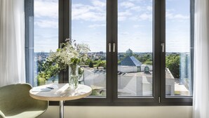 Een kamer met een groot raam, een tafel met een bloemenvaas en een stoel.