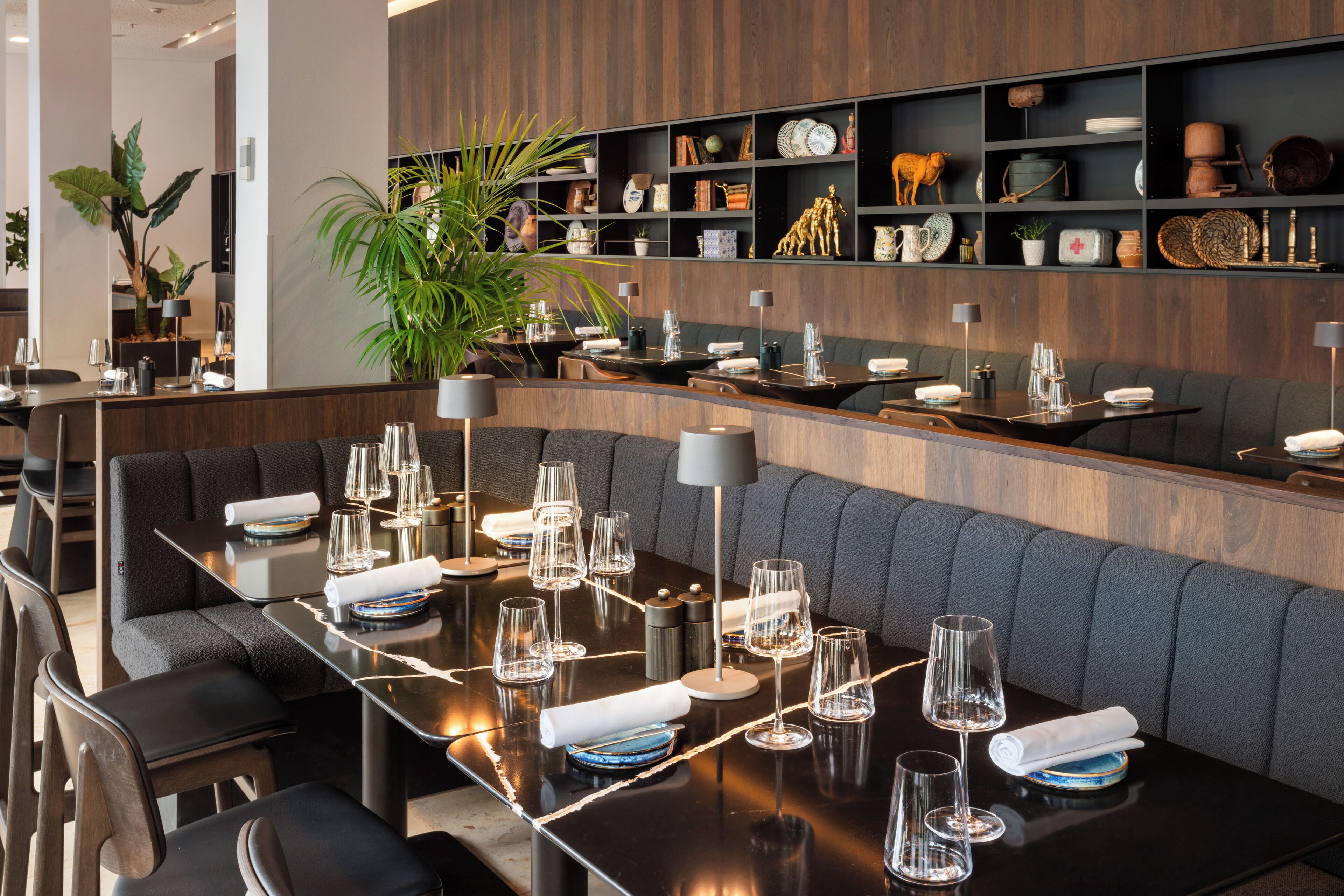 Un restaurant moderne doté d’une longue table à manger, de sièges confortables et de divers objets décoratifs disposés sur des étagères.