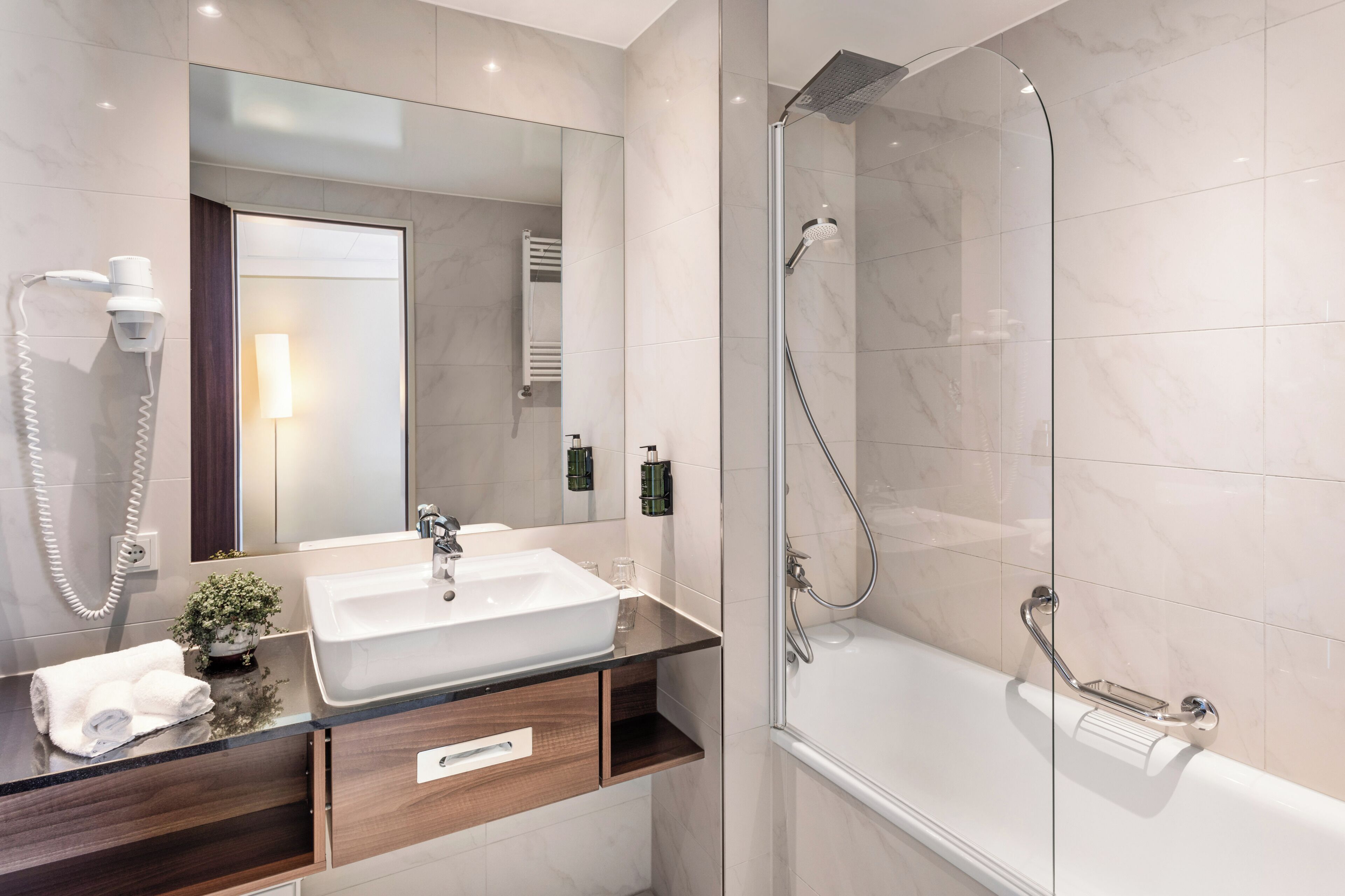 Un baño moderno con ducha de vidrio, lavamanos blanco y espejo sobre él.