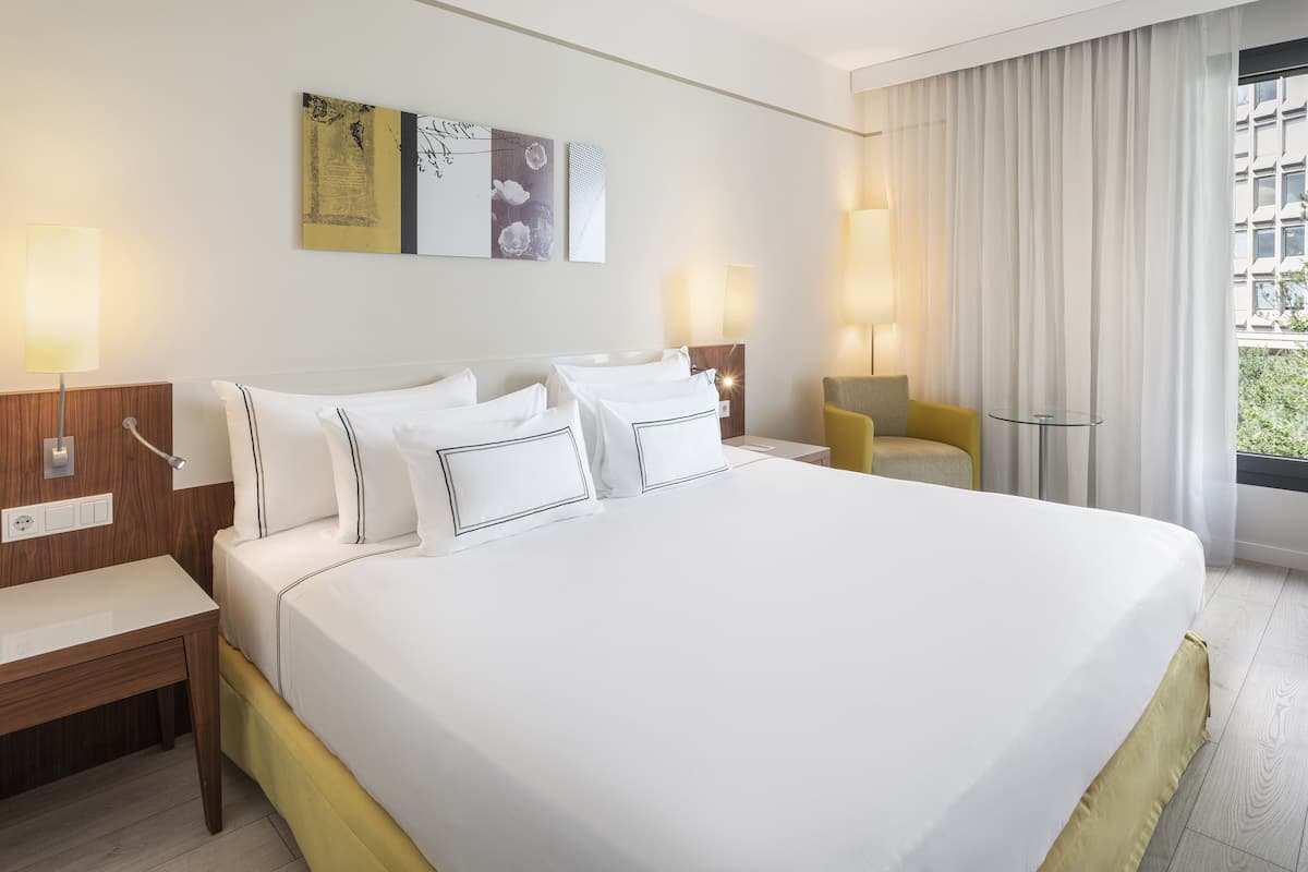 Una habitación de hotel con una cama grande, mesitas de noche, una silla y una ventana con cortinas.