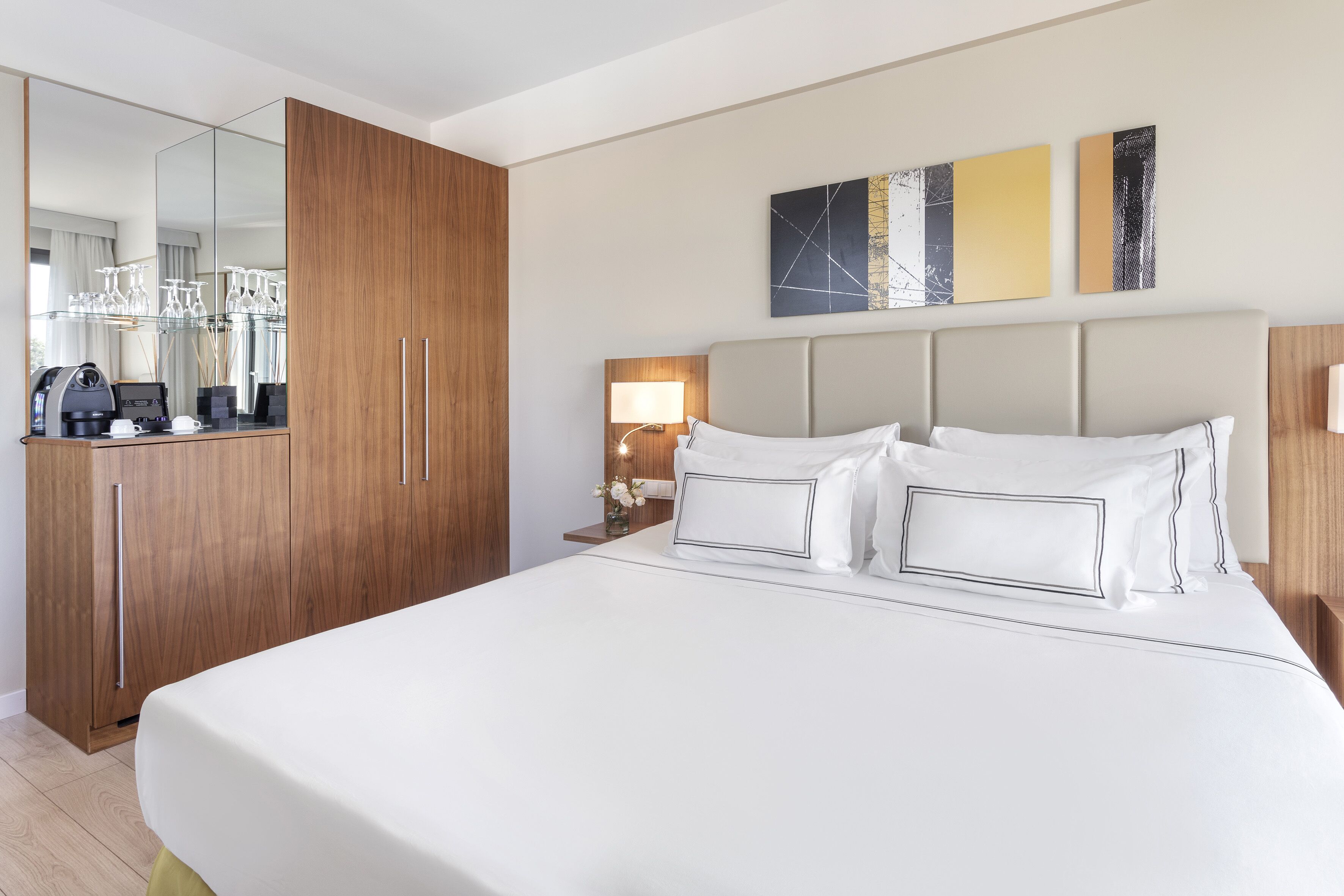 A hotel room with a large bed, wooden wardrobe, bedside table with a lamp, and a mirror.